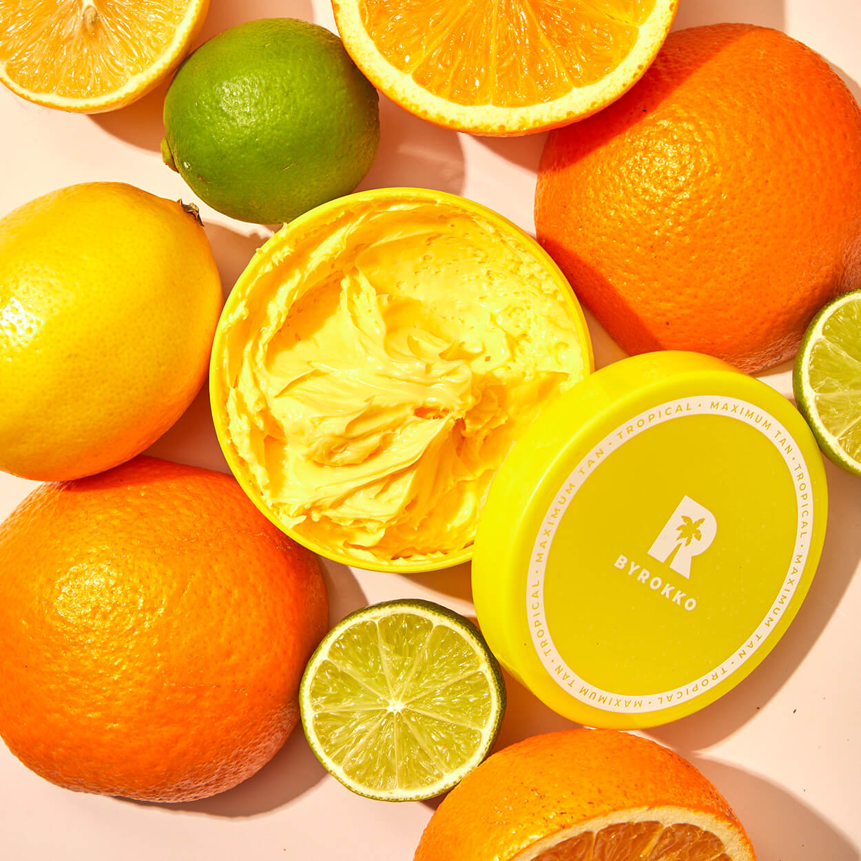 An open package of Byrokko Shine Brown Tropical tanning cream beside oranges, limes, and lemons.